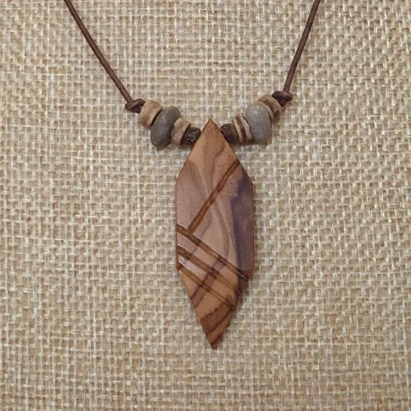 Detaillierte Frontalansicht des Anhängers aus Olivenholz der Holzkette #15 "Chevalier Chevron" mit Blick auf die Elemente der Kette bestehend aus Kokosperlen und selbstgebohrten Fluss-Steinen